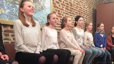 En gruppe unge piger sidder i en hal og smiler til kameraet