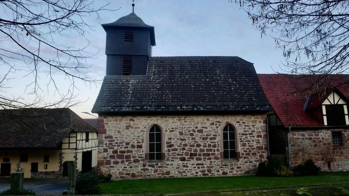 Steinkirche mit hohem Turm und daneben ein Gebäude mit rotem Dach.