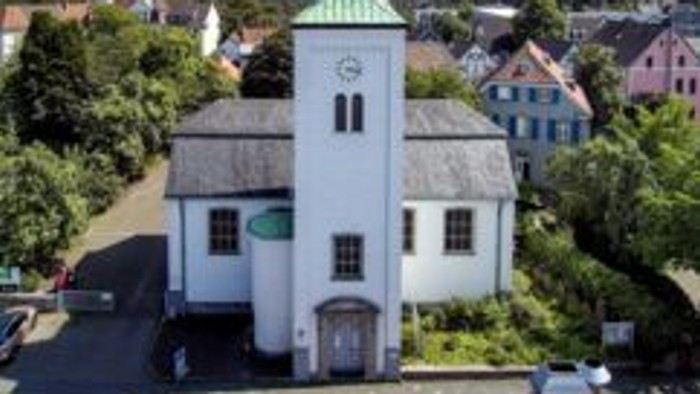 Luftaufnahme einer malerischen weißen Kirche mit grünem Turm in einer kleinen, idyllischen Stadt.