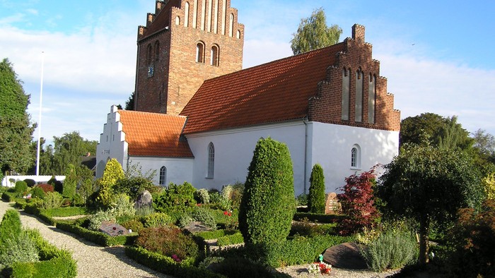 En smuk kirke med rød tag og omgivelser af grønne planter og træer