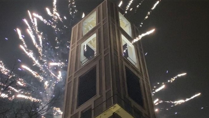 Feuerwerk explodiert am Himmel über einem hohen Ziegelturm mit Uhr.