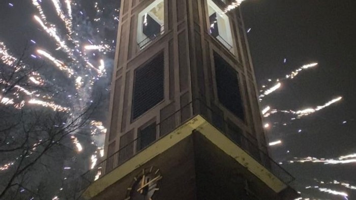 Feuerwerk explodiert am Himmel über einem hohen Ziegelturm mit Uhr.