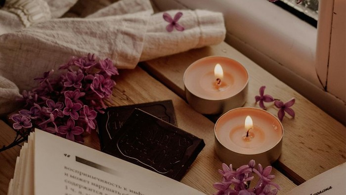 Zwei brennende Kerzen auf einem Holztisch mit Blumen und einem Buch