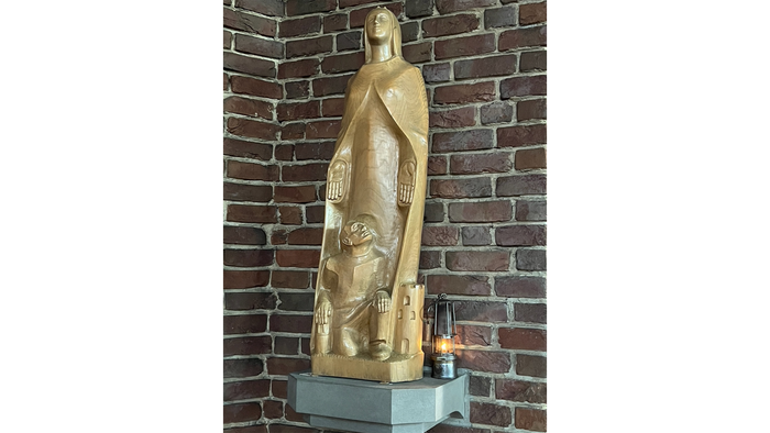 Die goldene Statue einer Frau mit Kind vor Ziegelmauer.