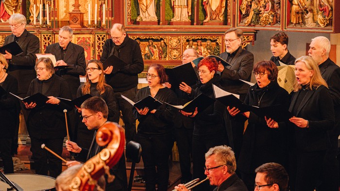 Ein Chor singt in einer Kirche, begleitet von Musikern mit Notenblättern
