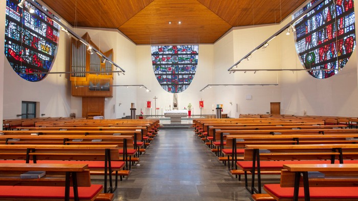 Leere Kirche mit Holzgestühl und bunten Fensterglasmalereien