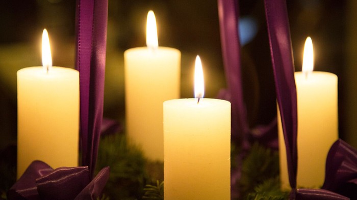 Fire tændte stearinlys omgivet af lilla sløjfer og grønne blade.