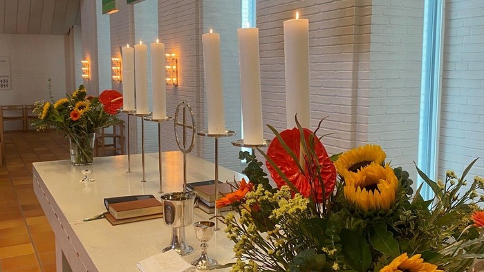 Bord med blomster, lysstake og brød i lys og farverig kirke
