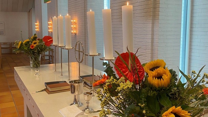 Bord med blomster, lysstake og brød i lys og farverig kirke