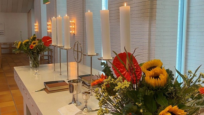 Bord med blomster, lysstake og brød i lys og farverig kirke