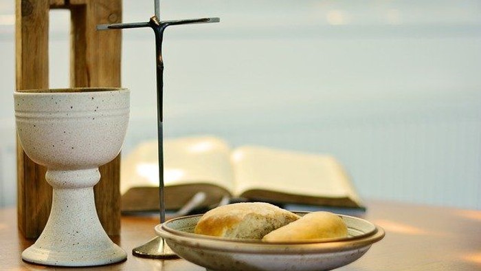 Ein Kelch, ein Kreuz und ein offenes Buch liegen auf einem Tisch