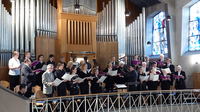 Ein Chor probt oder tritt in einer Kirche mit einer großen Orgel und bunten Glasfenstern auf.