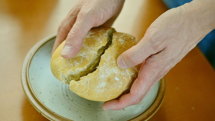 Eine Hand hält ein mit Puderzucker bestäubtes Gebäck über einem Teller.