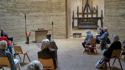 Eine Gruppe älterer Menschen sitzt in einem Raum mit steinernen Wänden und hört einem Redner zu.