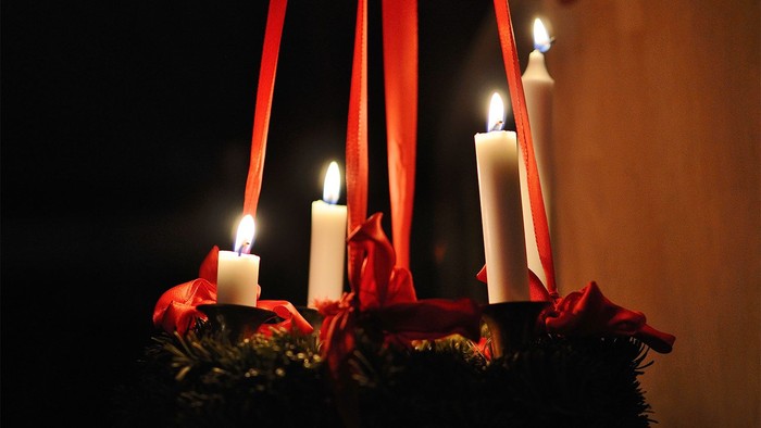 En julekrans med tre lysende lysekønge og røde bælter.