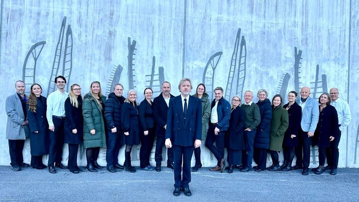 Eine Gruppe von Menschen posiert vor einem Hintergrund mit skizzenhaften Hochhäusern.