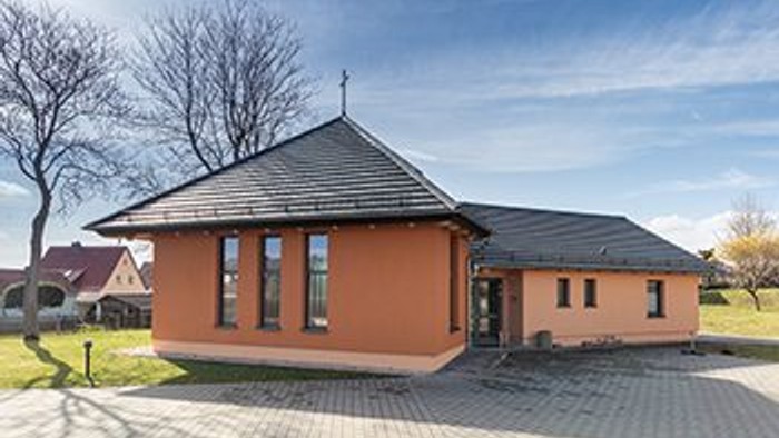 Ein modernes, oranges Haus mit schwarzem Dach und großen Fenstern steht auf einem gepflasterten Grundstück.