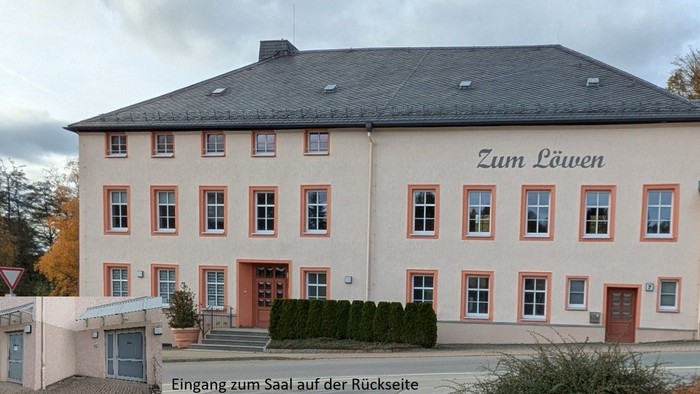 Ein großes zweigeschossiges Gebäude mit dem Schild *„Zum Löwen“*, umgeben von Grünflächen und einem bewölkten Himmel.