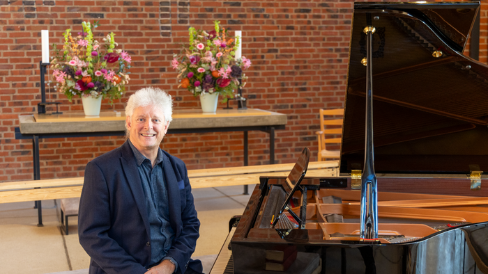 Mand, der sidder ved et klaver med blomster i baggrunden.