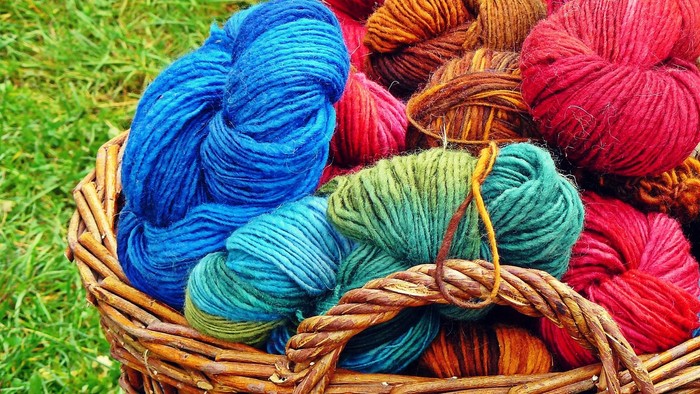 En wicker-basket med bunte garnspinder i blå, rød og grøn