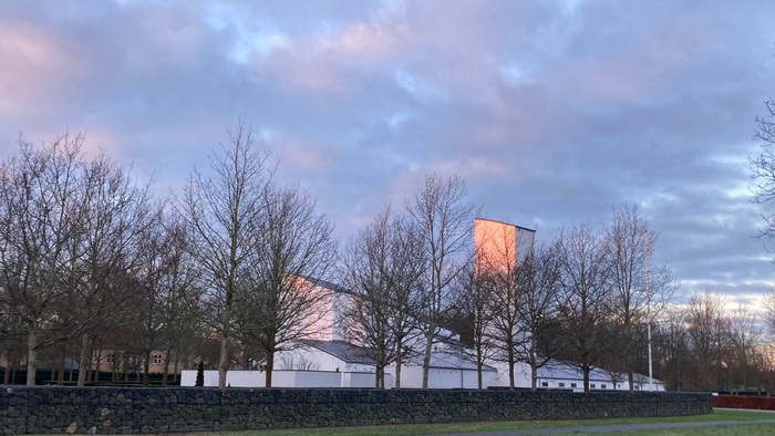 Tornbjerg Kirke set fra øst med lav rødligt genskin af morgensol på kirketårnet igennem nøgne træer