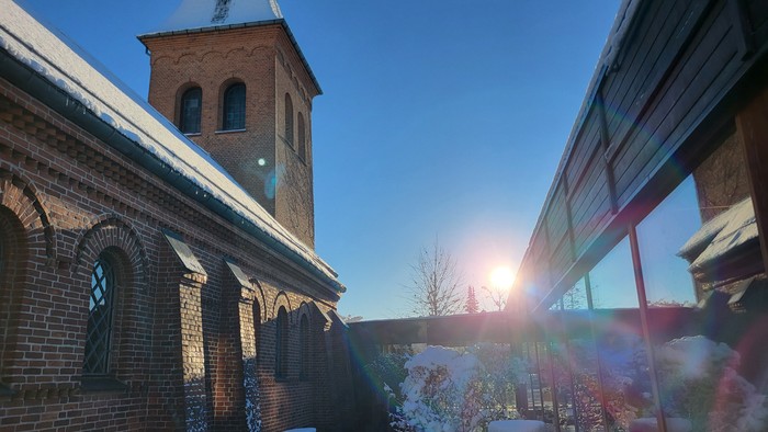 En kirke med tårn og klokke i sneklædt landskab ved solopgang