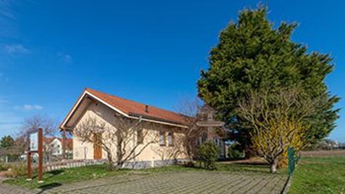 Ein großes Haus mit rotem Dach und einem Baum davor unter klarem blauem Himmel.