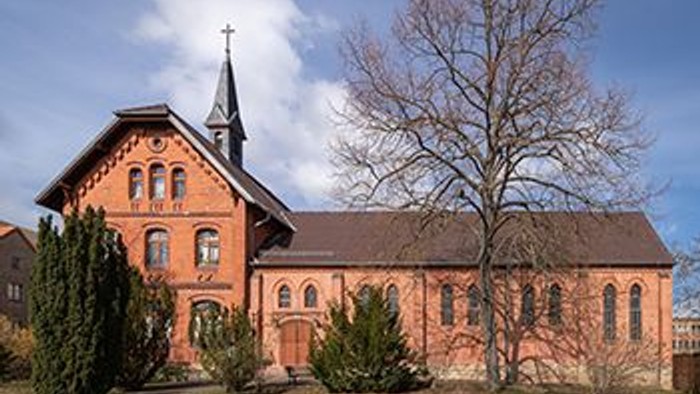 Ein rotes Backsteingebäude mit spitzem Turm und zwei Bäumen davor