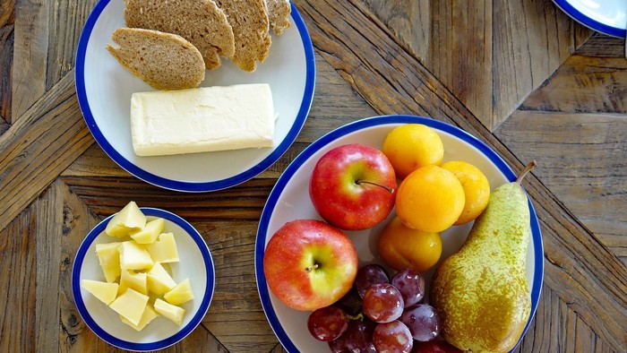Auf dem Holztisch stehen Schalen mit Brot, Käse und Obst.