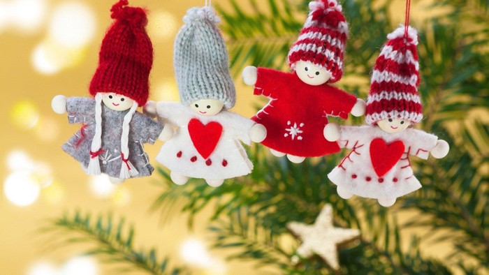 Vier Weihnachtsbaumschmuck-Figuren in Winterkleidung hängen an einem Tannenbaum