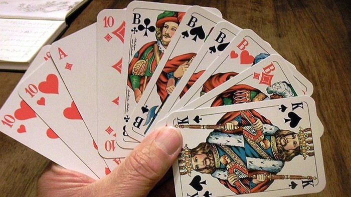 Eine Hand hält mehrere Spielkarten mit verschiedenen Bildern und Zahlen