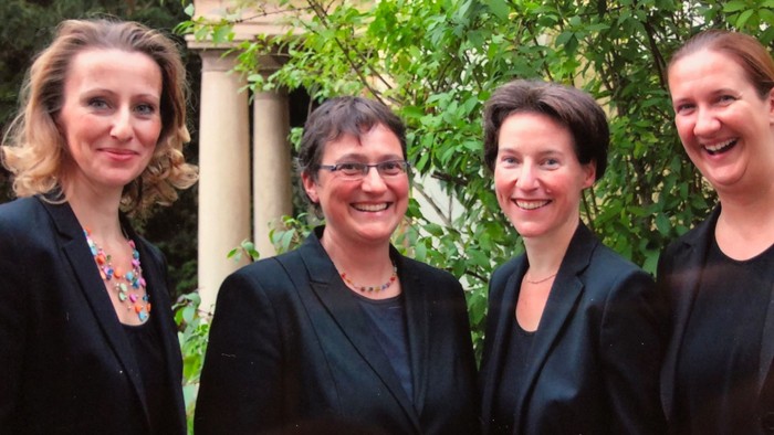 Vier Frauen in Anzügen lächeln vor grünem Hintergrund