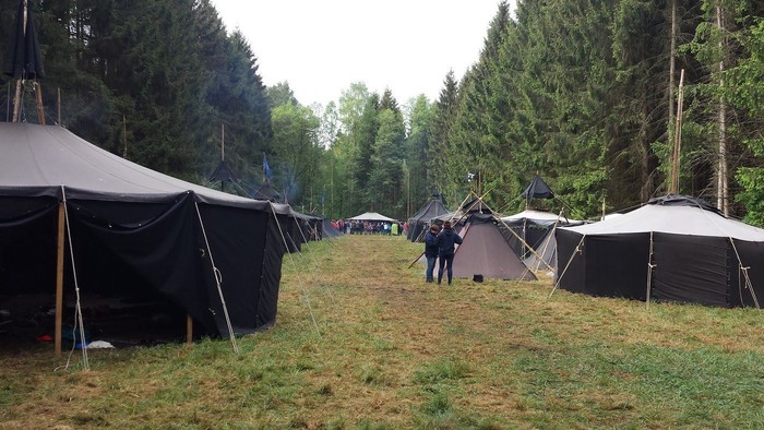 Mehrere Zelte, die in einer grasbewachsenen Fläche zwischen Bäumen aufgestellt sind.