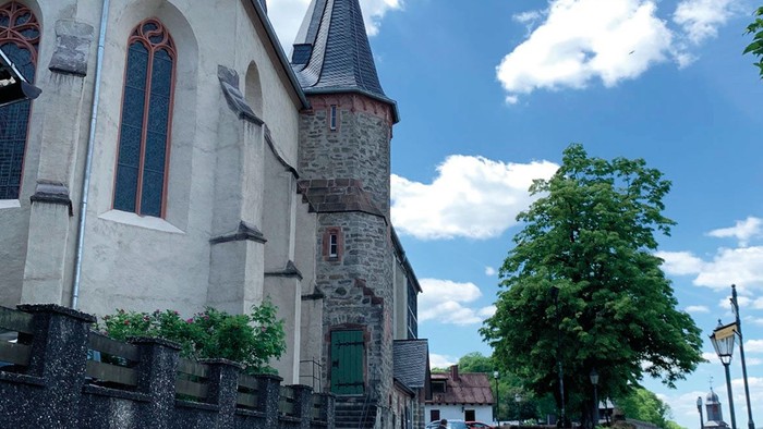 Altes Kirchengebäude mit Turm und Menschen auf Kopfsteinpflasterstraße