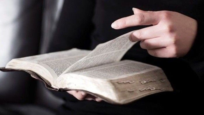 Person, der holder en åben bog med en finger, der peger på teksten.