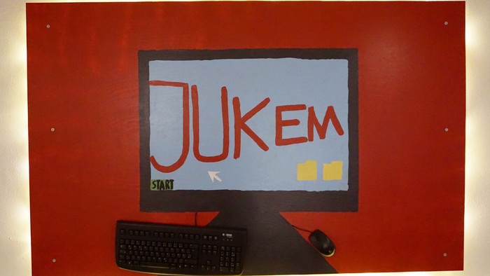 Das Bild zeigt einen roten Monitor mit der Aufschrift "JUKEM" und einer Tastatur davor.