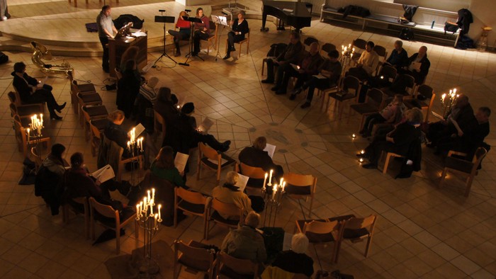 Eine Gruppe von Menschen sitzt in einem Kreis und hält Kerzen, während einige Musiker in der Mitte spielen.