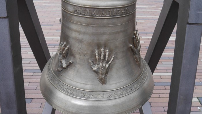 Die Glocke ist mit zwei Händen und einer Inschrift verziert.