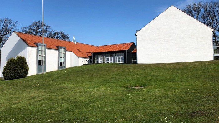 Hvidt hus med rødt tag og dansk flag på en bakke