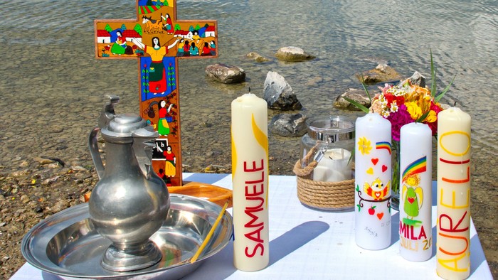 Religiöse Gegenstände wie Kerzen, ein Kreuz, ein Krug und ein Korb am Wasserufer.