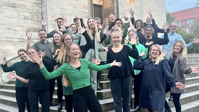 En gruppe unge mennesker står sammen på træerne foran et stenhus og poser til kameraet.