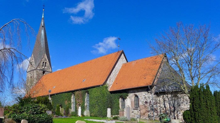 Kirchengelände mit spitzem Turm und rotem Dach unter blauem Himmel