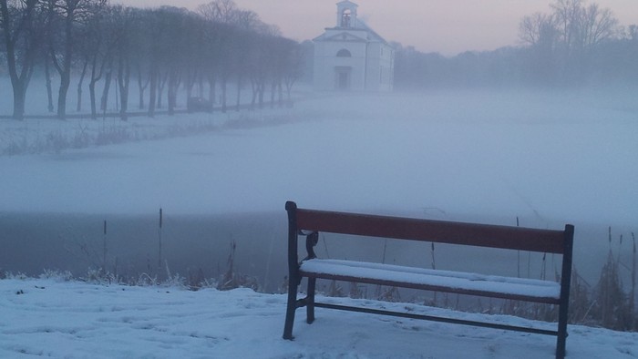 En snebelægtet park med en alene benk og en kirke i baggrunden.