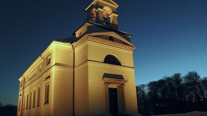 En belyst gul kirke med tårn og klokke mod nattehimmel