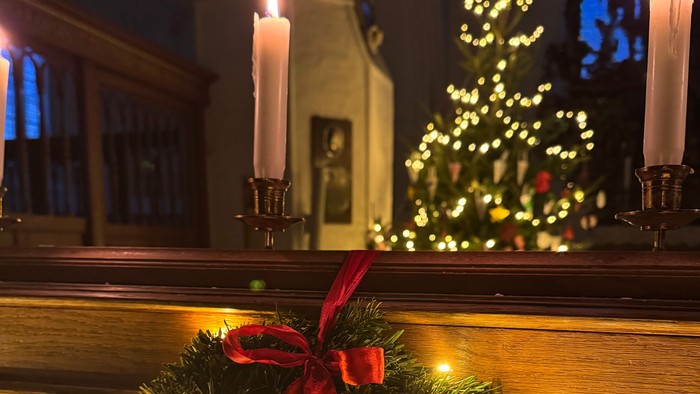 En juletidskærede med lys og rød bue foran en lyset kælderkammer med lysende juletræ og lyse candlesticks