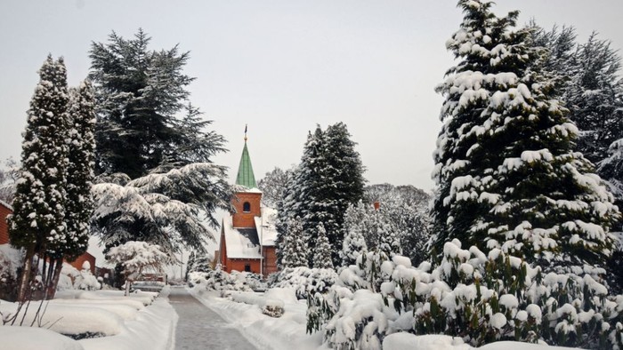 En snedækket vej med en rød og hvid kirke med grøn tårnspire.