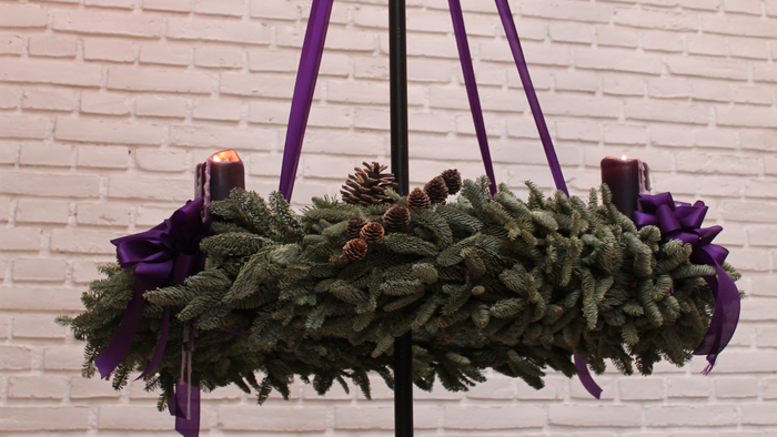 En hængende julekrans med lilla bånd og lys på en mur