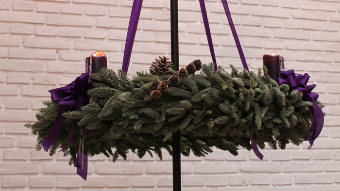 En hængende julekrans med lilla bånd og lys på en mur