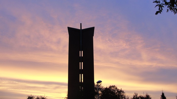 En høj klokketårn mod en rødgul skyscene ved solnedgang