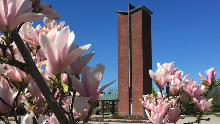 En høj murstenstårn med skråt tak og blomster i forgrunden